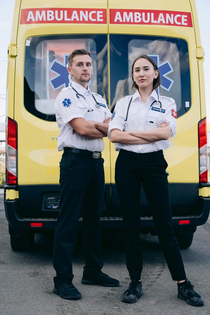 Two paramedics confidently stand in front of a yellow ambulance, showcasing teamwork and readiness.