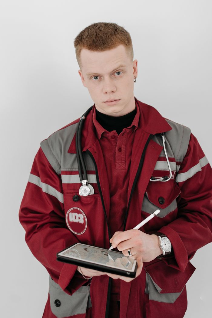 Male paramedic in uniform using a tablet device with a stethoscope around his neck.